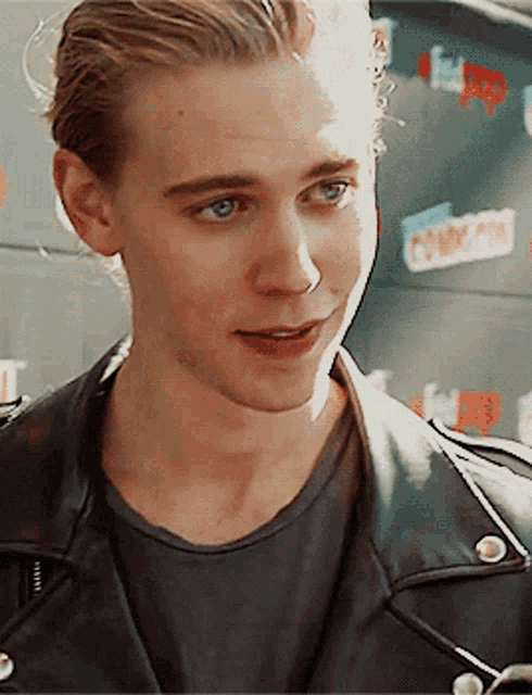 a young man wearing a black leather jacket stands in front of a wall that says comic con