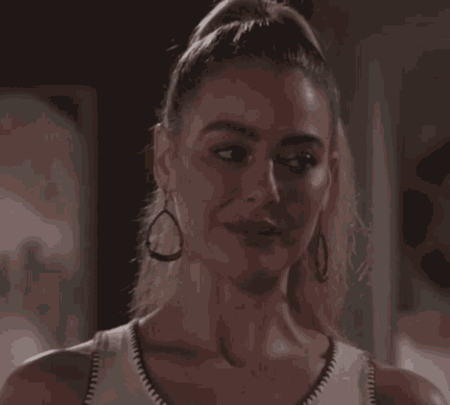 a woman wearing a white tank top and hoop earrings