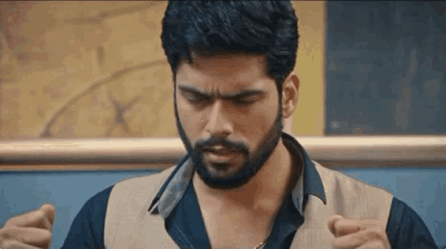 a man with a beard is wearing a black shirt and a tan vest and making a funny face .