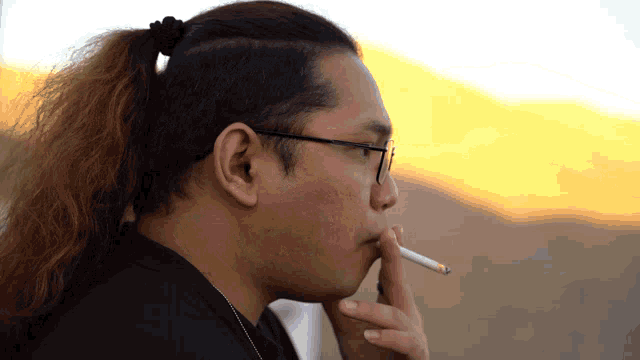 a man with glasses smoking a cigarette with a mountain in the background