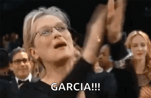 a woman wearing glasses is raising her hands in the air while sitting in a crowd of people .