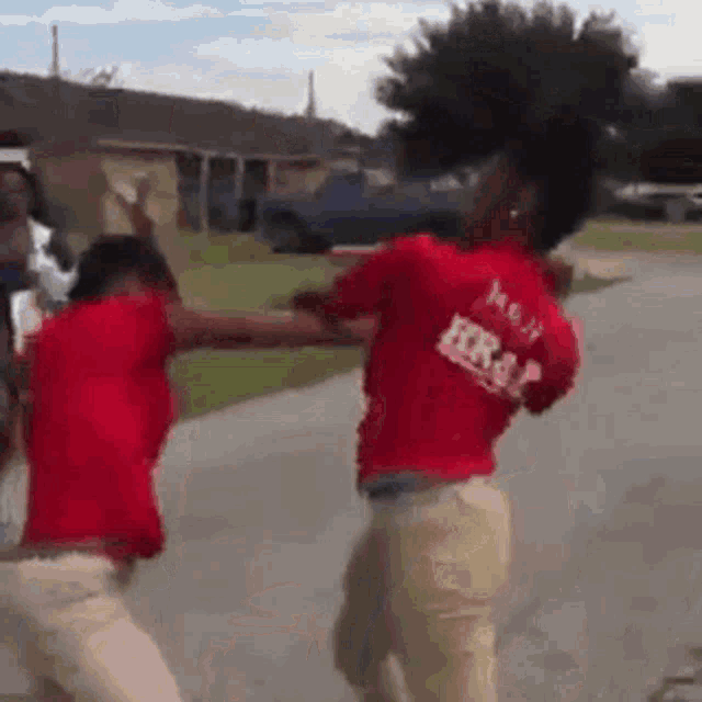 two people in red shirts are fighting each other on the street .