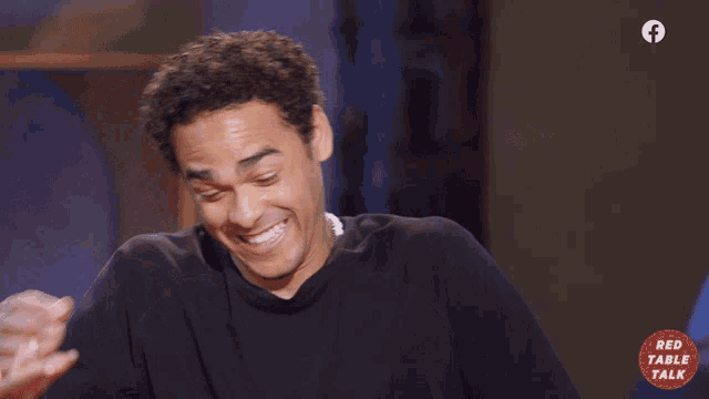 a man is laughing in front of a red table talk sign