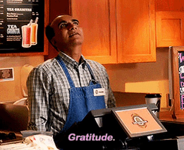 a man in an apron stands behind a counter that says gratitude on it