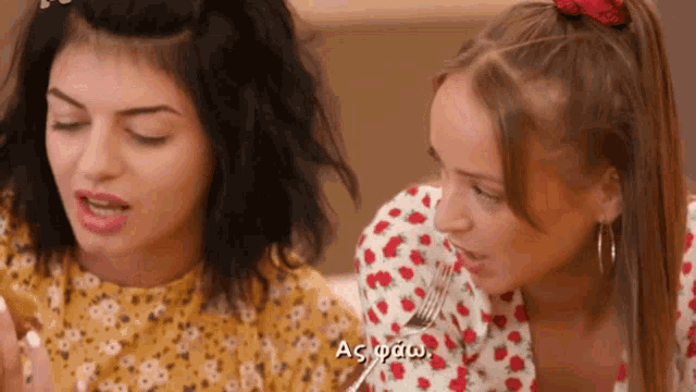 two girls are sitting next to each other and one of them is holding a fork in her mouth while the other looks on