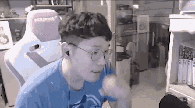 a man wearing glasses is sitting in a pink and white gaming chair .