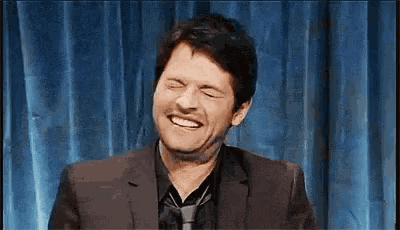 a man in a suit and tie is laughing with his eyes closed .