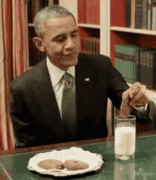 a man in a suit is sitting at a table with a plate of cookies and a glass of milk