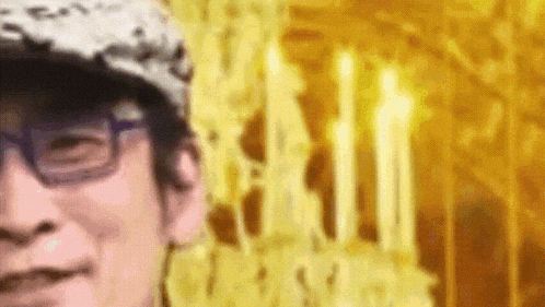 a man wearing glasses and a hat is smiling in front of a yellow background