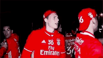 a man wearing a fly emirates jersey is standing in a crowd