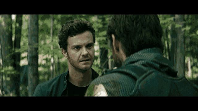 two men are standing in the woods and talking