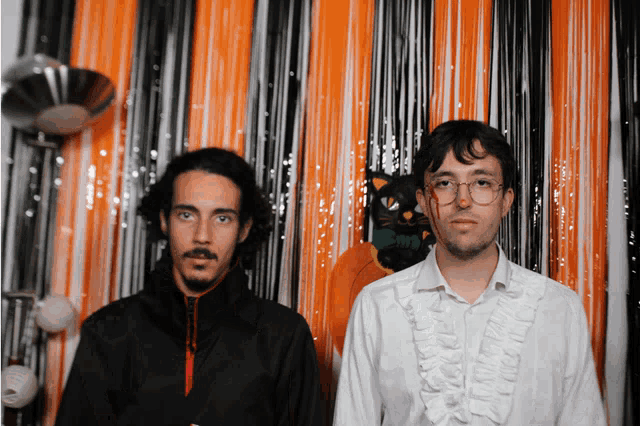 two men are standing in front of an orange curtain