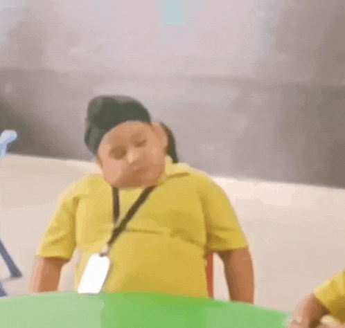 a little boy in a yellow shirt and black hat is sitting at a table .