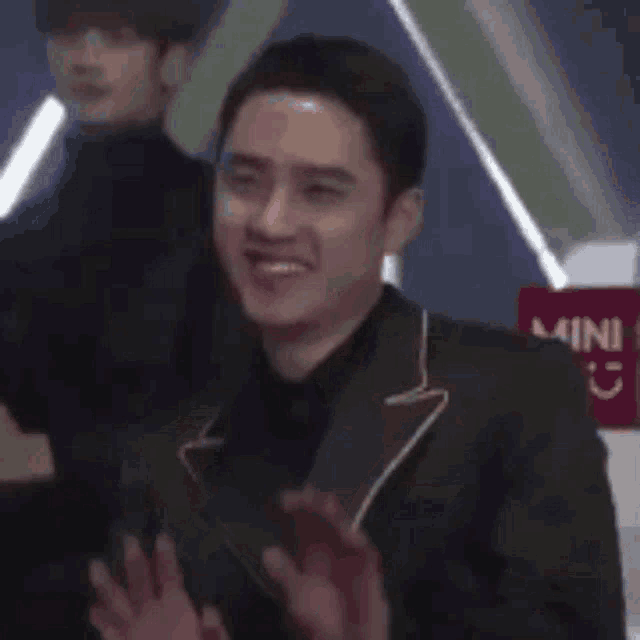 a man in a black jacket is smiling and waving his hands .