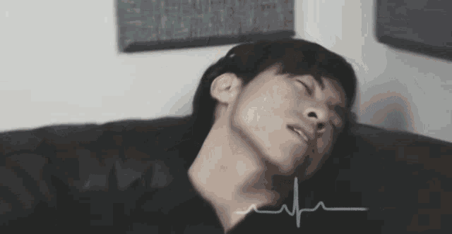 a young man is laying on a couch with his eyes closed and a heartbeat line behind him .