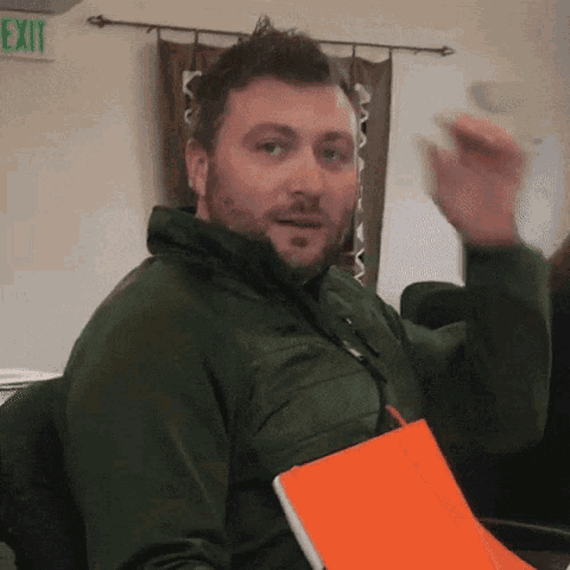 a man in a green jacket is sitting in front of a green exit sign
