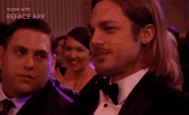 a man in a tuxedo is sitting next to a woman in a crowd .