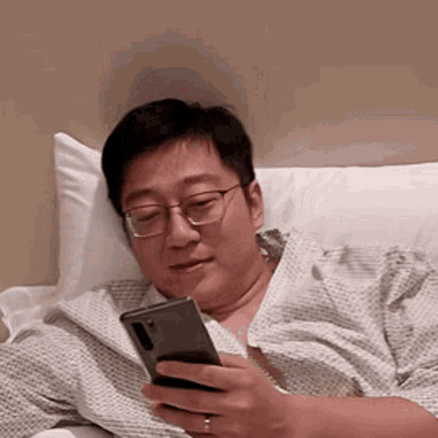 a man wearing glasses is laying on a bed looking at his cell phone