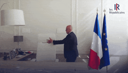 a man in a suit is standing in front of two flags and a sign that says les republique