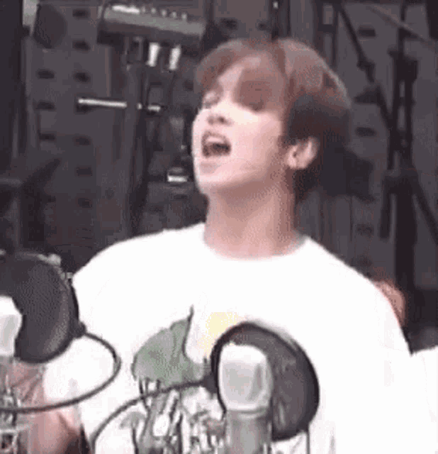 a young man is singing into a microphone in front of a microphone .