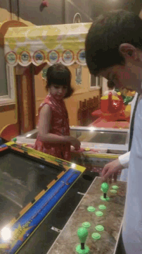 a man and a little girl are playing a video game that says ' arcade ' on it