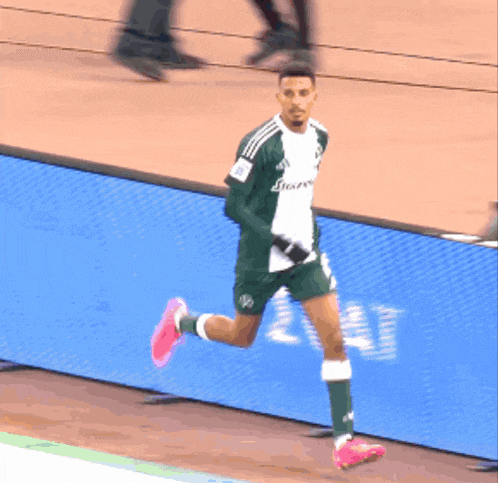 a soccer player wearing a green and white adidas shirt is running