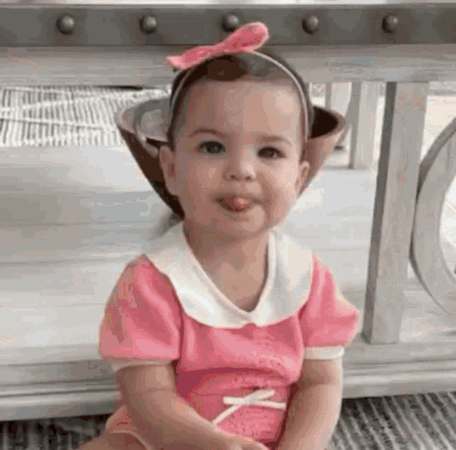 a little girl in a pink dress and headband is sticking out her tongue .