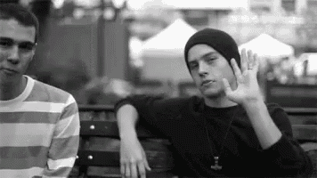 two young men are sitting on a bench in a park .