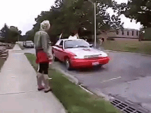 a woman is standing next to a red car on the side of the road .