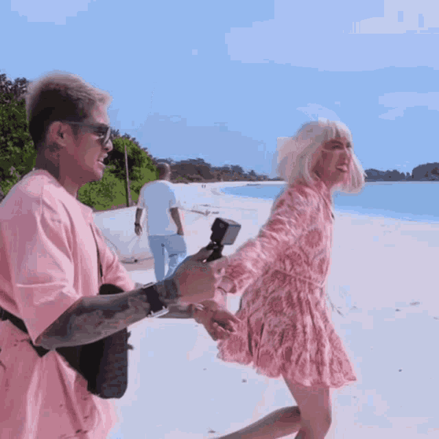 a man in a pink shirt is holding the hand of a woman in a pink dress on a beach
