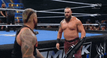 two wrestlers are standing in a wrestling ring and one of them is holding a bat