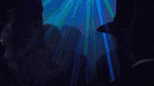 a man in a hat stands in a dark room with a blue light behind him
