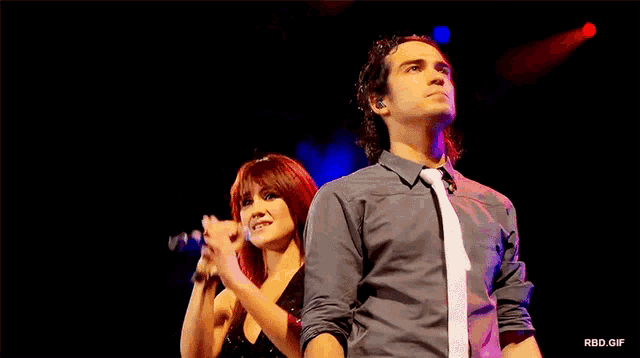 a woman singing into a microphone next to a man in a tie on stage