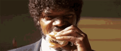 a man with curly hair is eating a hamburger with cheese