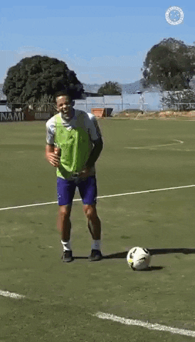 a man in a green vest is kicking a soccer ball on a soccer field .