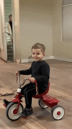 a young boy is riding a red tricycle on a wood floor