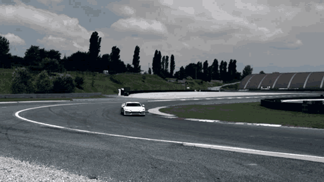 a white car driving on a race track with a red building in the background