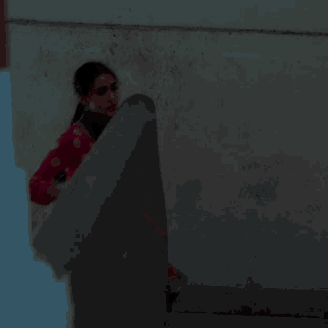 a woman in a red dress is standing in front of a wall holding her skirt up .