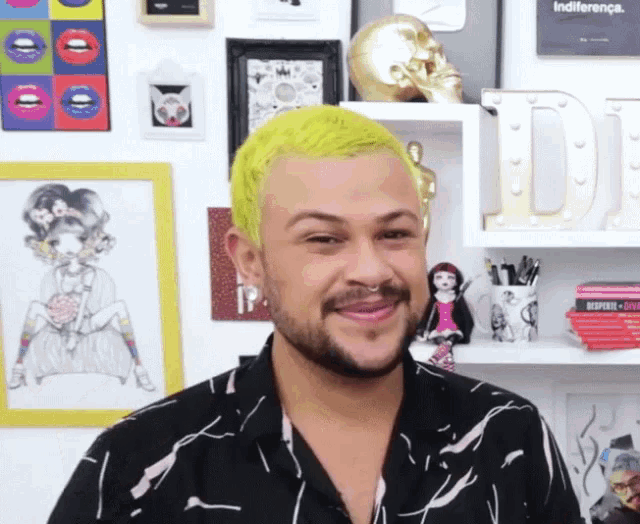 a man with bright yellow hair is smiling in front of a shelf with a sign that says indiferenca