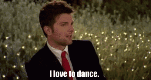 a man in a suit and tie is sitting in front of a field of lights and saying `` i love to dance . ''