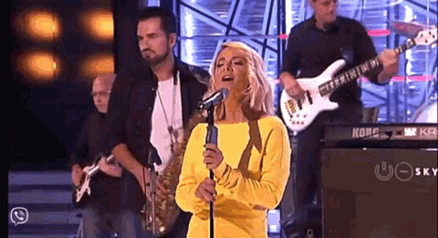 a woman in a yellow dress sings into a microphone with a korg keyboard in the background