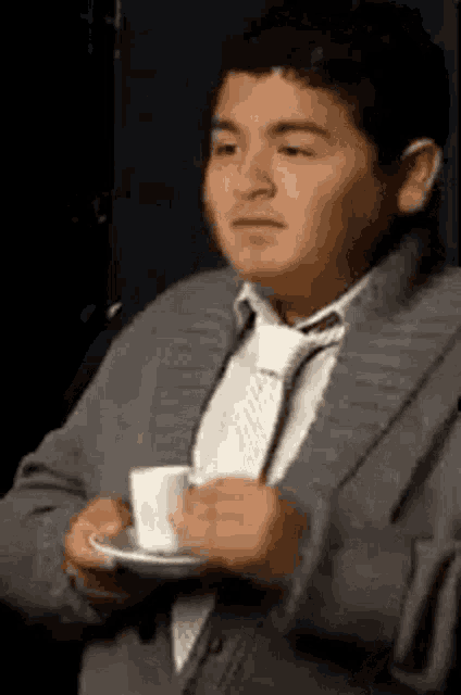 a boy in a suit and tie is holding a cup of coffee .