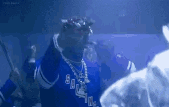 snoop dogg is wearing a blue jersey and holding a stick in a crowd of people .