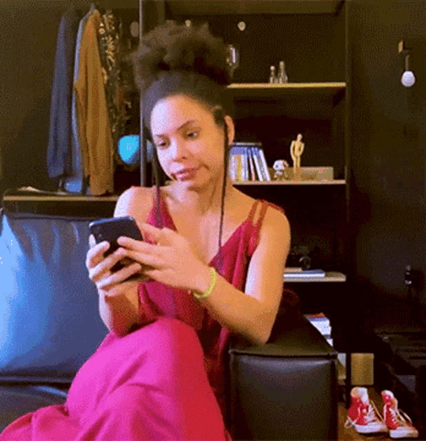 a woman in a red dress sits on a couch looking at her phone