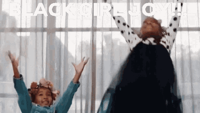 two little girls are dancing in front of a window with their arms in the air and the words black girl joy !