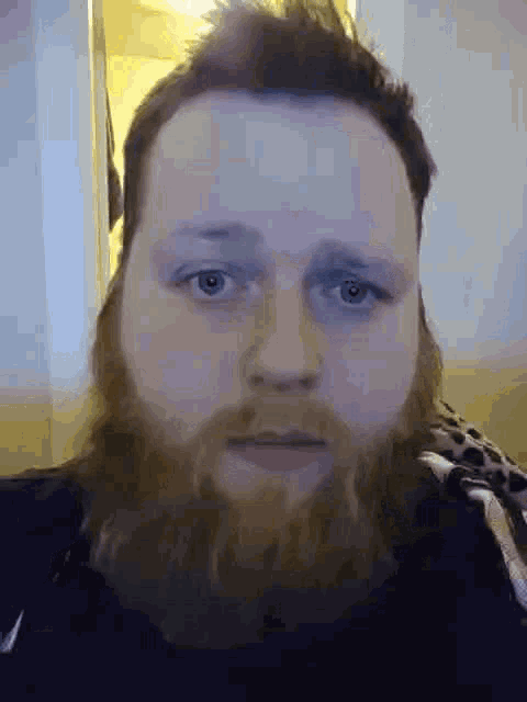 a man with a beard is looking at the camera with a serious look on his face