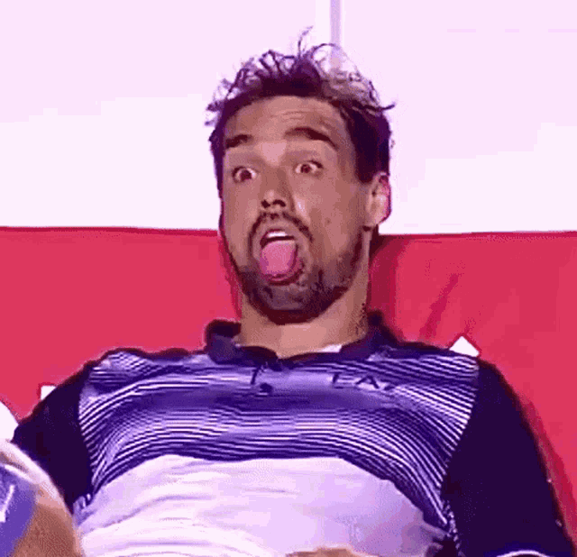 a man with a beard is sticking his tongue out while sitting on a red couch .