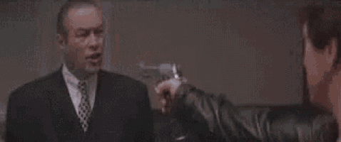 a man in a suit is pointing a gun at another man .