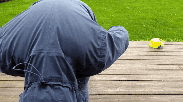 a person in a blue jacket is standing on a wooden deck looking at a yellow ball