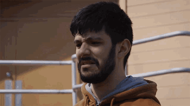 a man with a beard wearing a brown hoodie is making a funny face